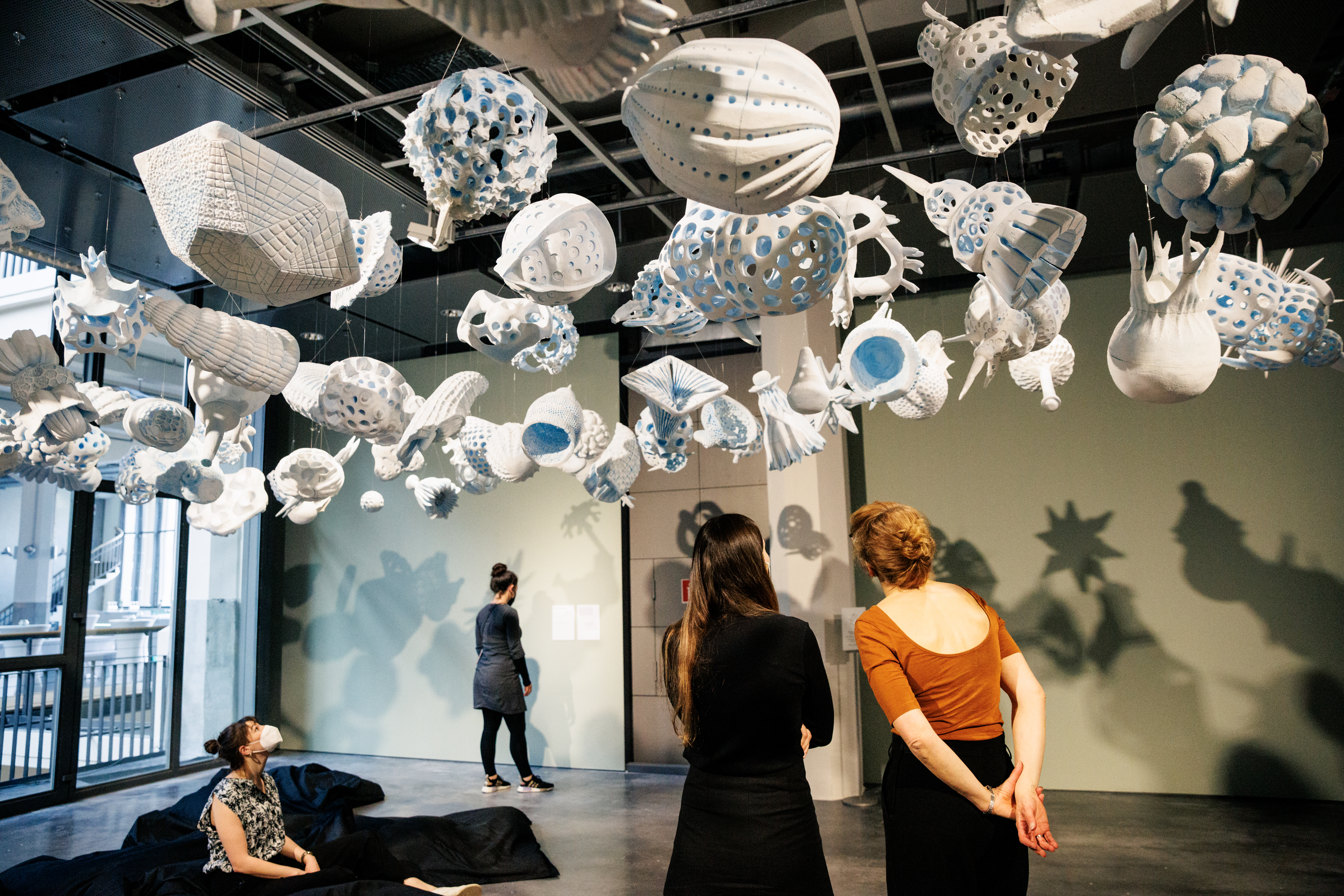 View of the exhibition »The Beauty of Early Life«. Several people look at the work of Reiner Maria Matysik »Radiolaria«.