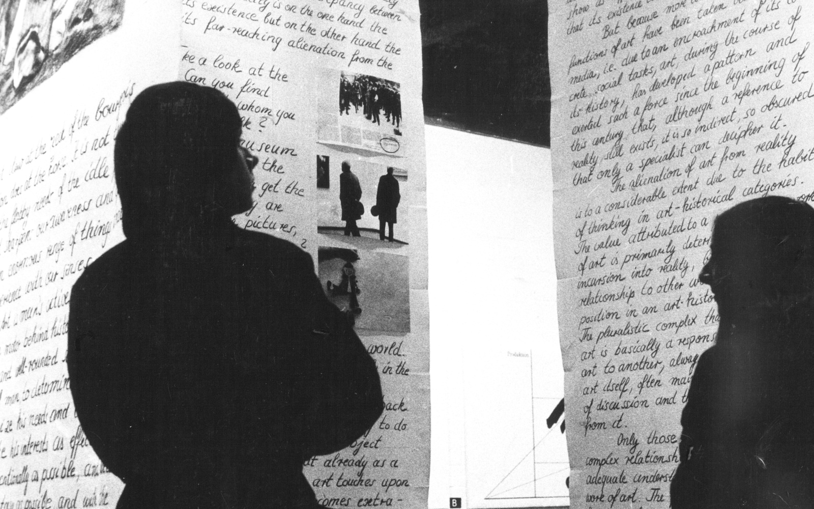 Two people are standing in front of sheets of fabric with lettering and pictures hanging from the ceiling.
