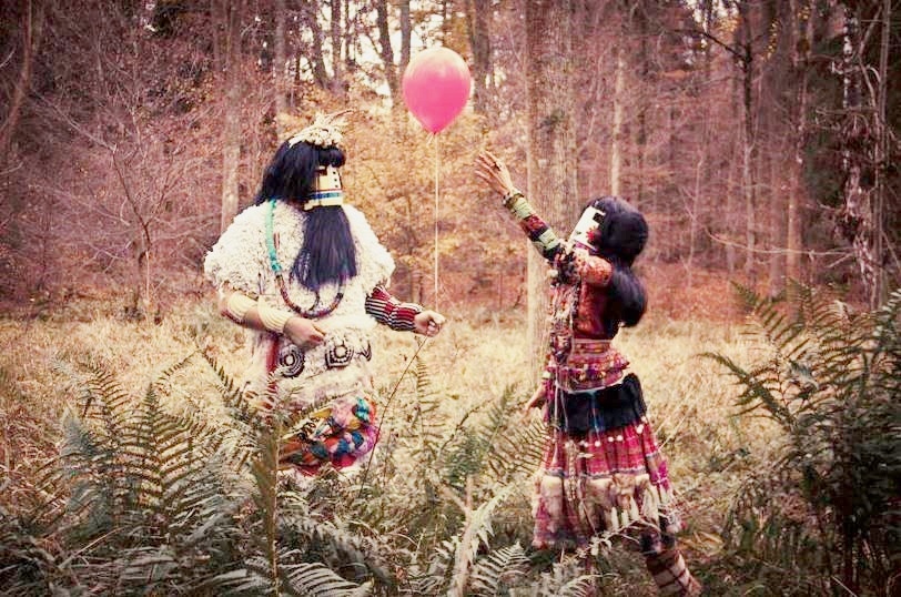Zwei kostümierte Personen spielen auf einer Waldlichtung mit einem rosa Luftballon