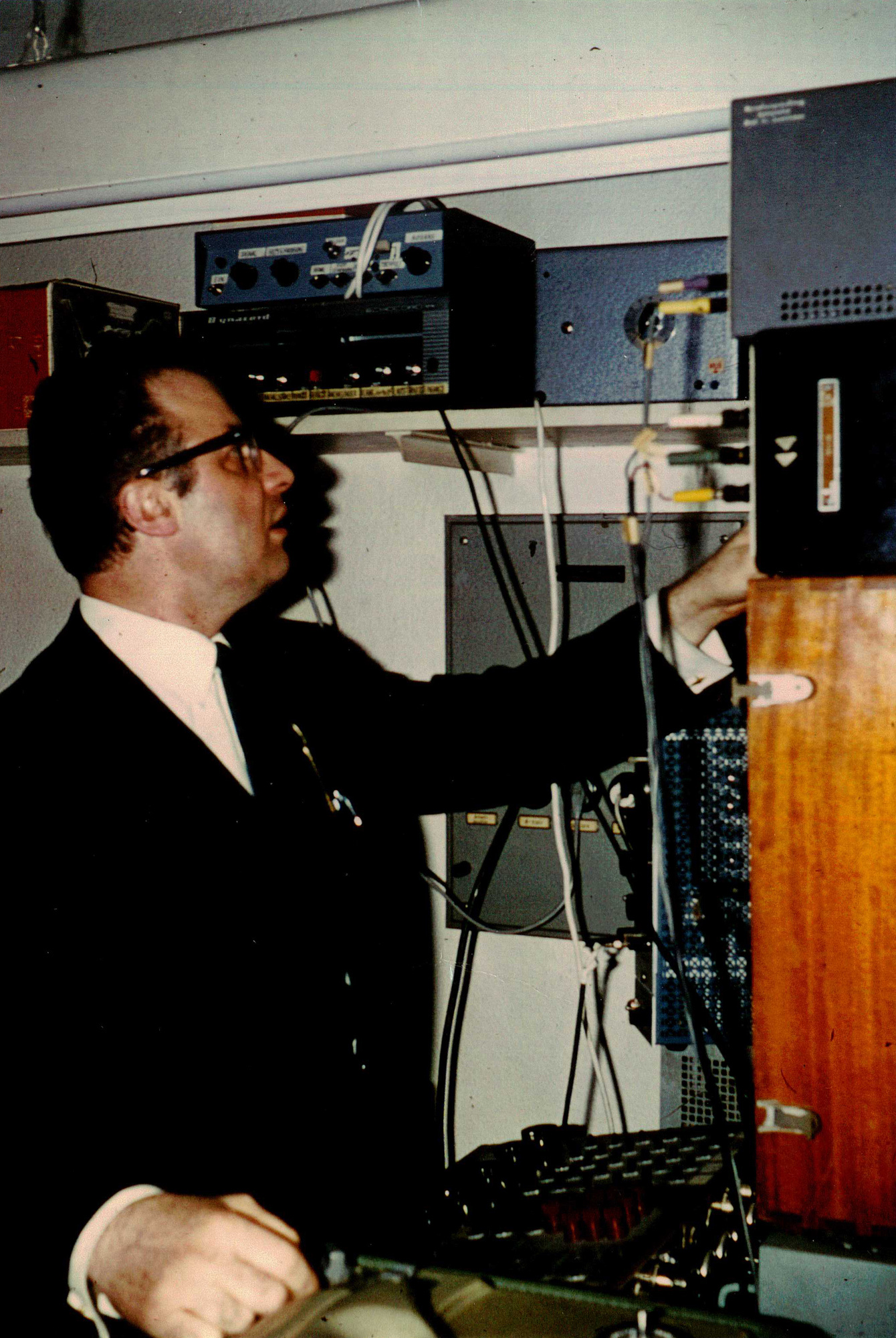 A man in a black suit and black horn-rimmed glasses served various electronic equipment.