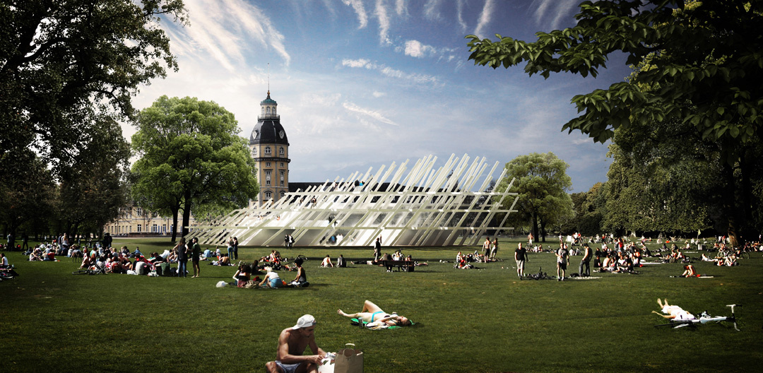 People lie on the grass in the sun. In the background, a large, open building