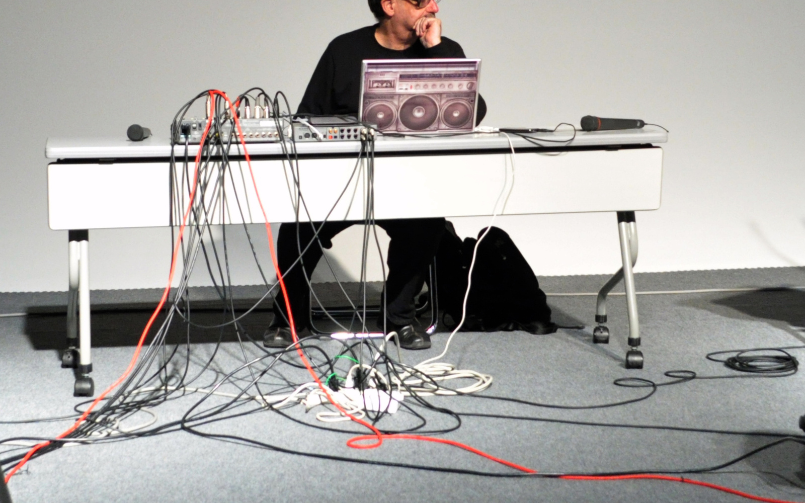 Ein Mann sitzt hinter einem Mischpult, unter dem Tisch verlaufen unzählige Kabel