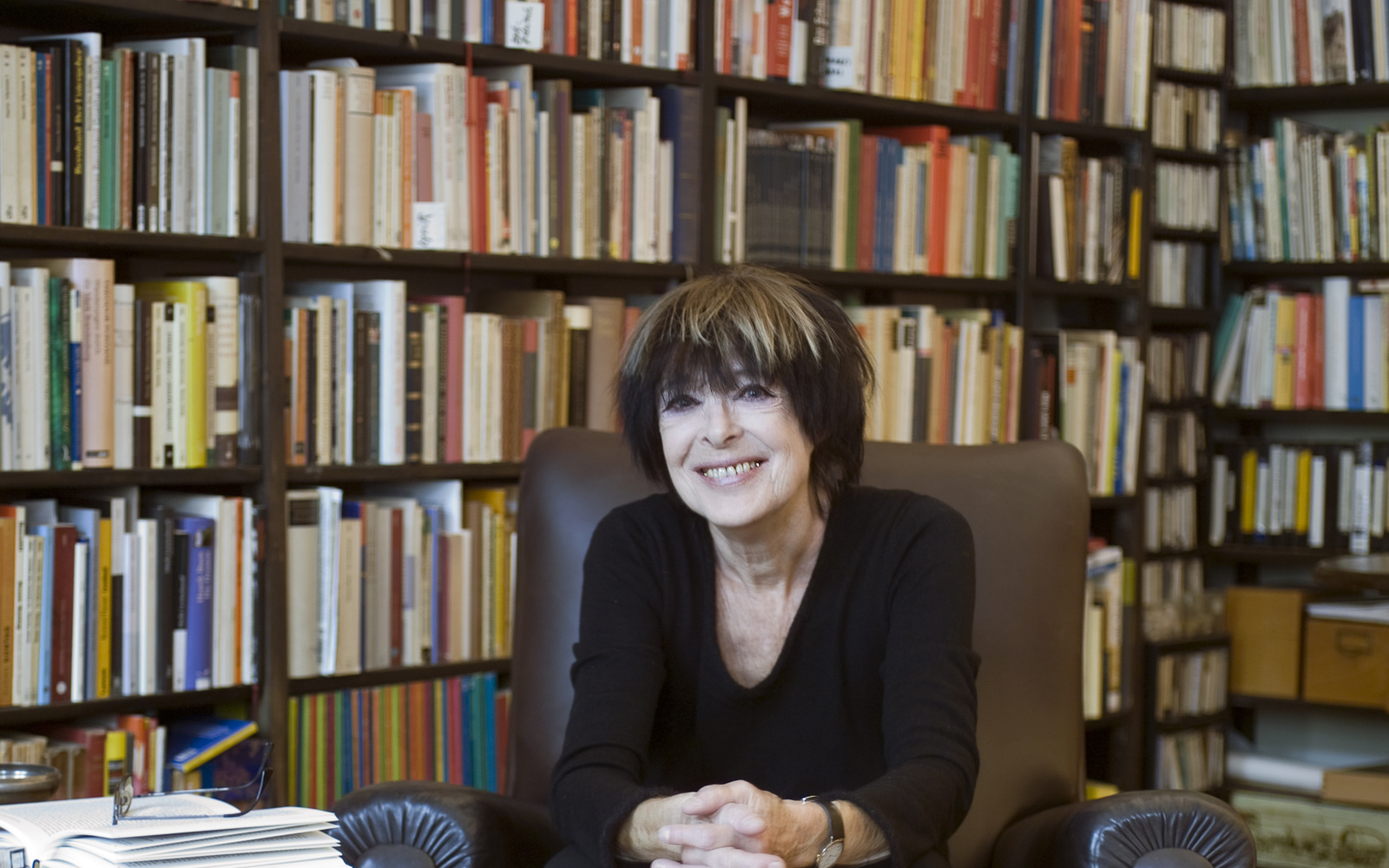 Eine Frau sitzt in einem Sessel vor einem großen Bücherregal.
