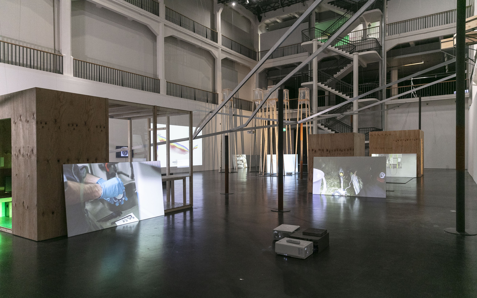 Blick in eine große Halle mit einem Gerüst und weißen Wänden auf denen Videos laufen.