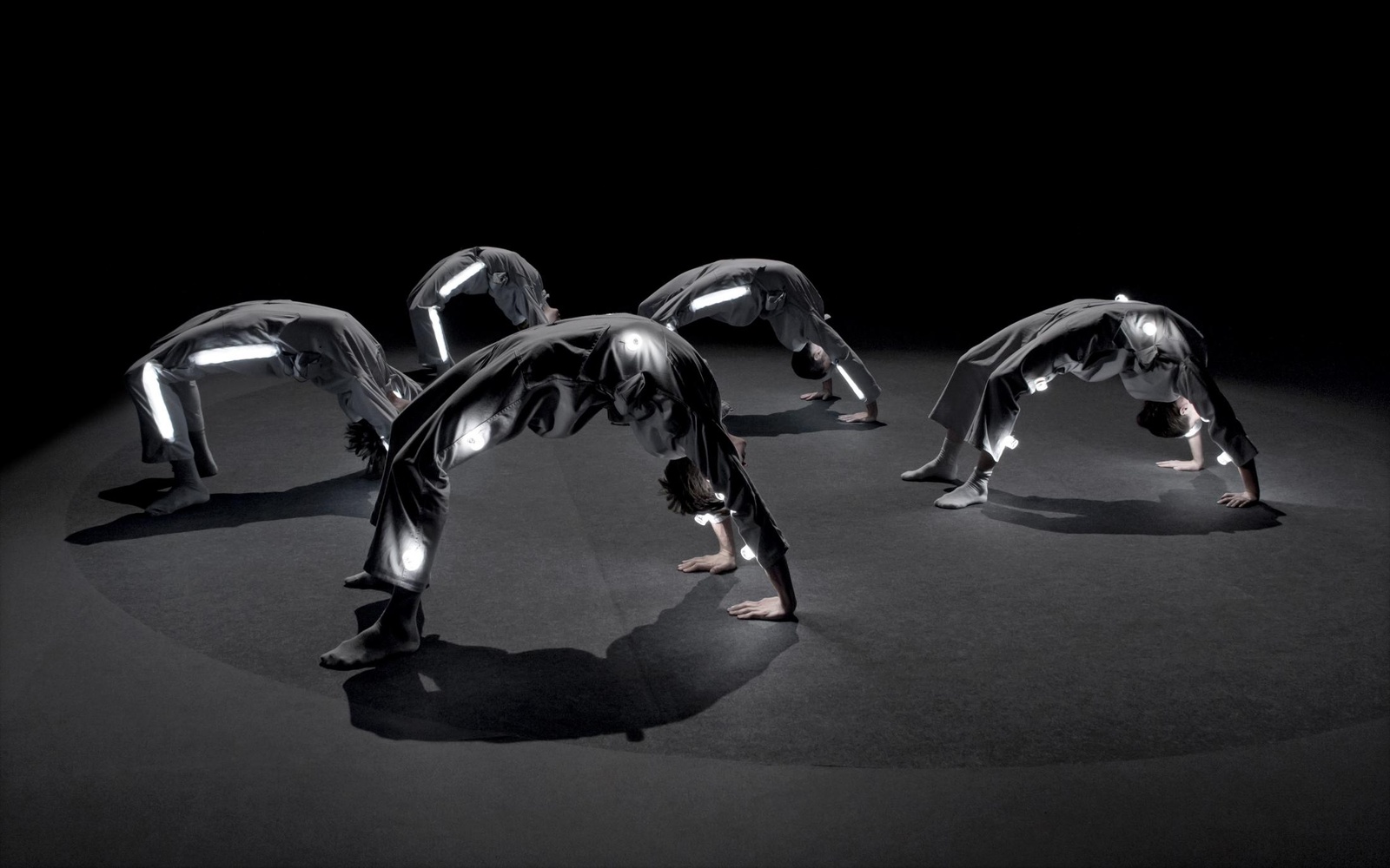 The picture shows five people building a bridge and dressed in grey. Light elements are integrated in her clothing