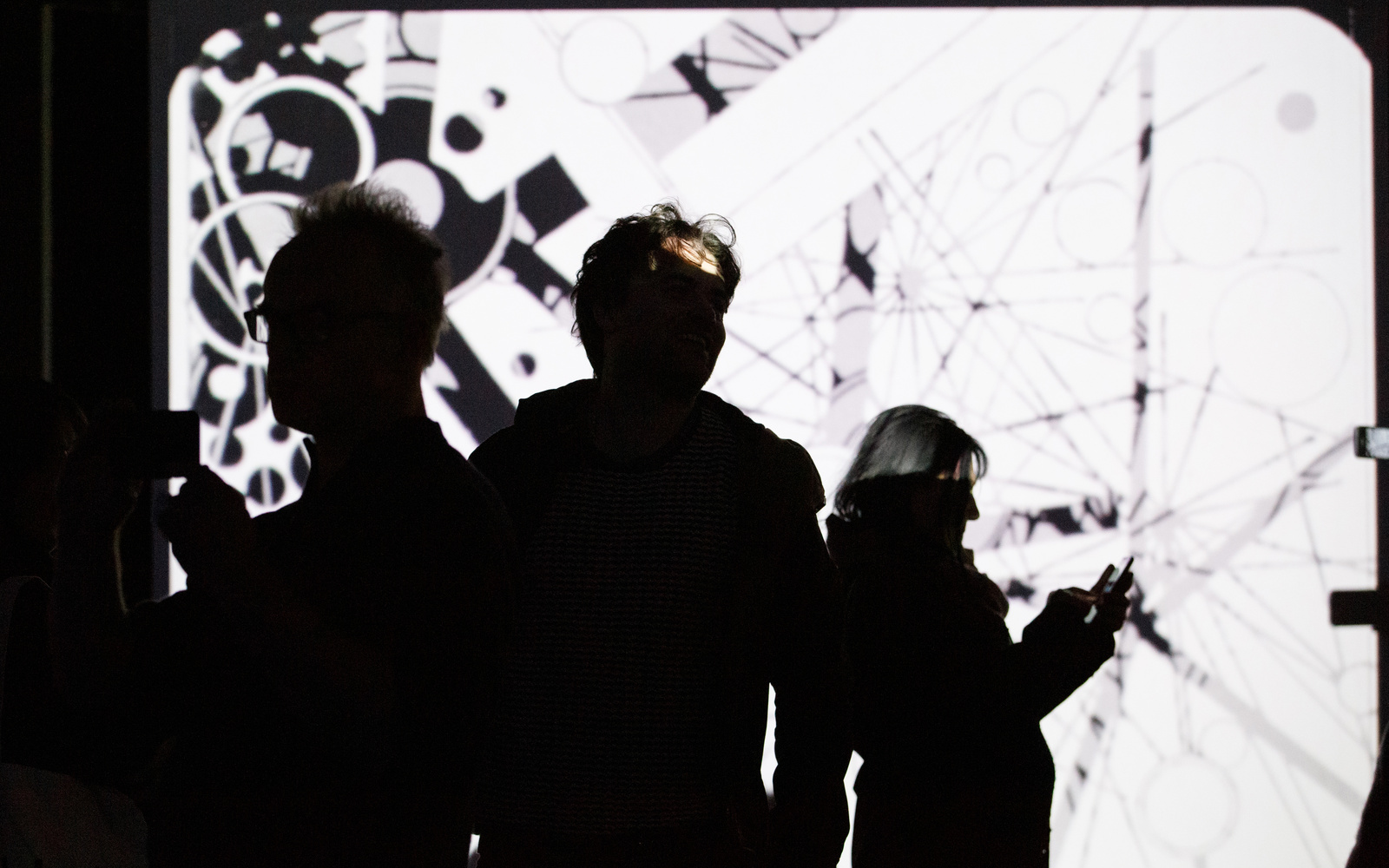 Photo of people in front of a projection screen with an abstract video in black and white - an impression of the exhibition »bauhaus.film.expanded« at the ZKM Karlsruhe.