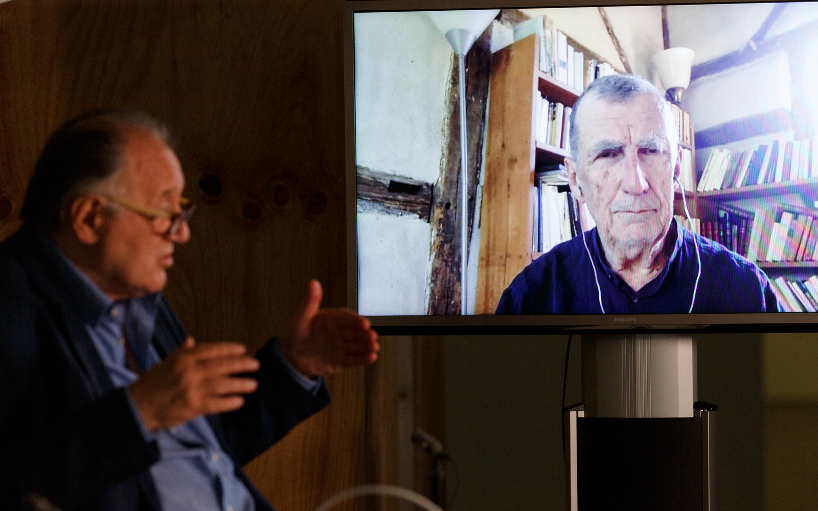 Peter Weibel sitzt vor einem großen Bildschirm auf dem Bruno Latour zu sehen ist.