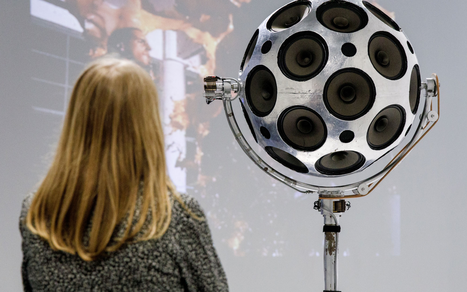 A woman stands in front of a silver sphere of loudspeakers