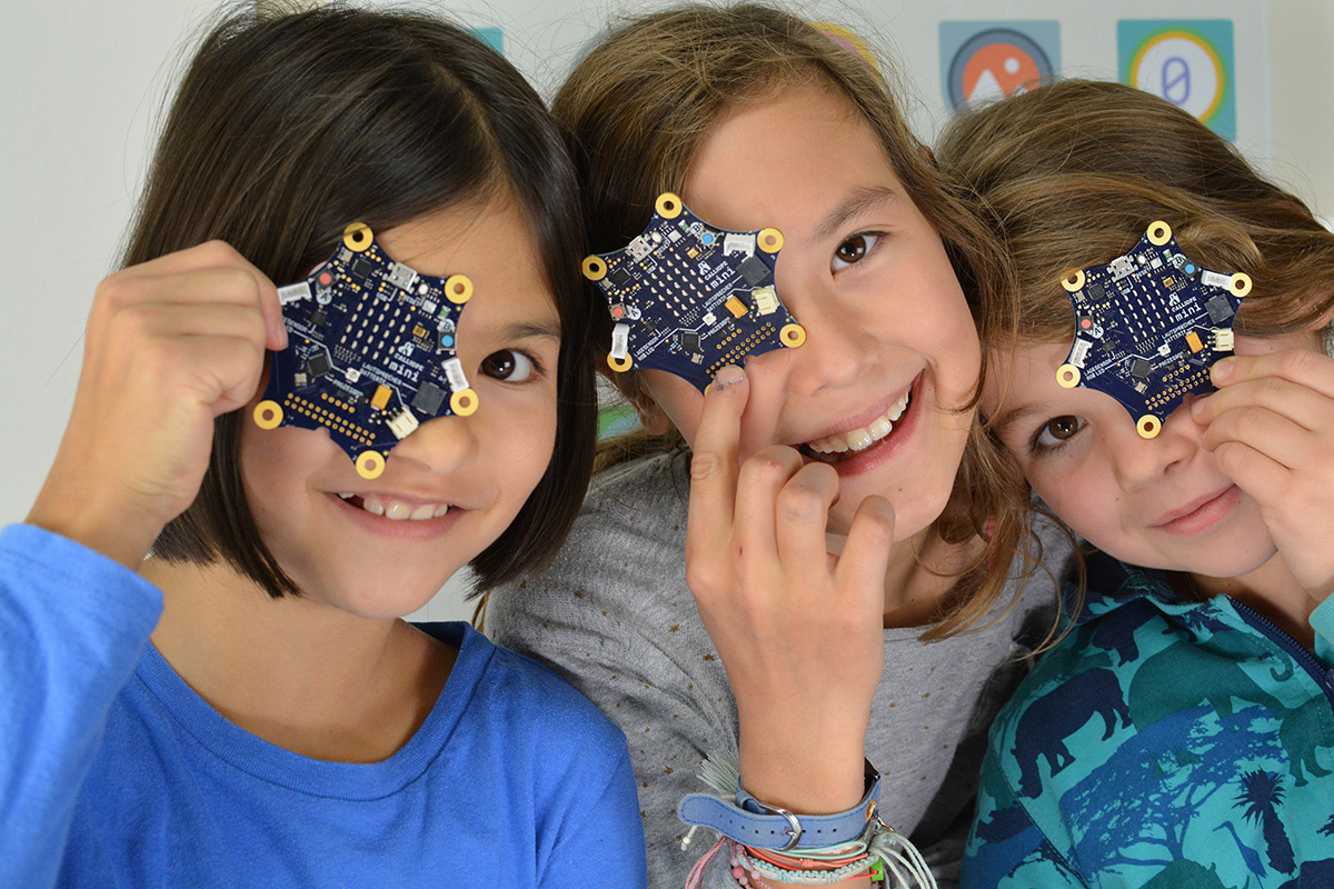 Photo of three young girls each holding a Calliope mini circuit board in front of their face.
