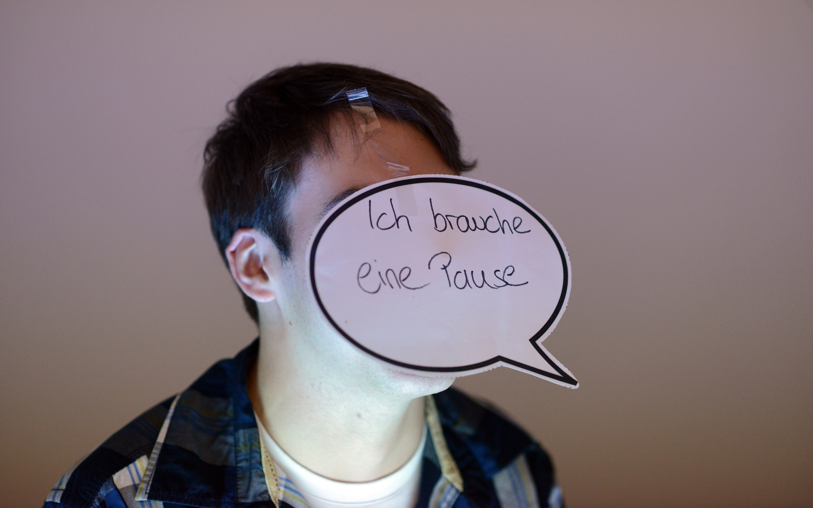 Ein Junge hat sich mit einer Sprechblase den Satz »ich brauche eine Pause« vor sein Gesicht geklebt.