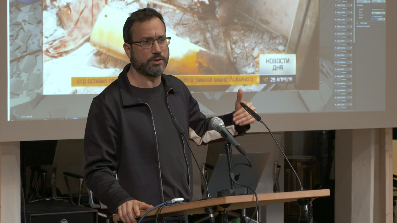 Eyal Weizman, ein Mann mit Bart und Brille hält einen Vortrag vor einer Leinwand..