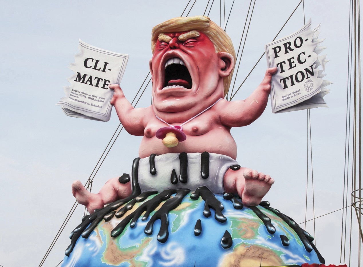 Eine Karikatur von Donald Trump zeigt diesen als Baby auf der Weltkugel sitzend, in der einen Hand ein Papier zu »Climate«, in der anderen ein Papier  zu »Protection«.  
