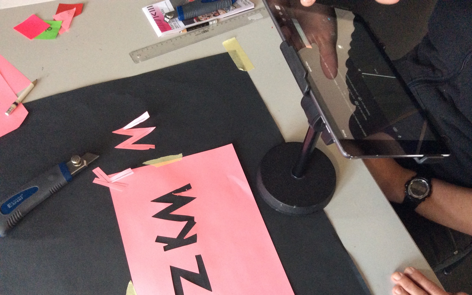 Auf einem Tisch ist das Equipment aufgebaut, welches für Legetrick benötigt wird. Außerdem ein Rosafarbenes Blatt Papier aus dem die Buchstaben ZKM ausgeschnitten wurden.