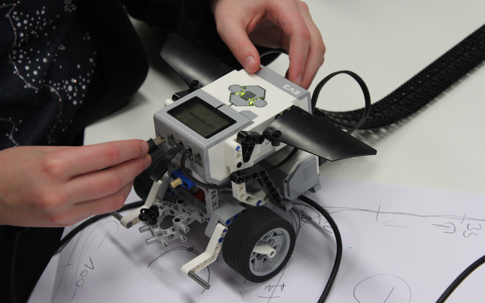 Ein Kind arbeitet an einem Lego-Roboter, gerade bringt es ein Kabel an der Vorderseite an.
