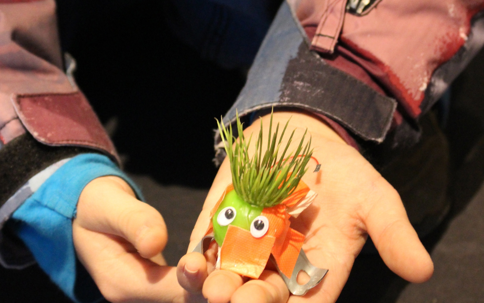 Kinderhände halten einen kleinen E-Käfer mit Kunstrasen als Haaren und Wackelaugen in die Kamera.