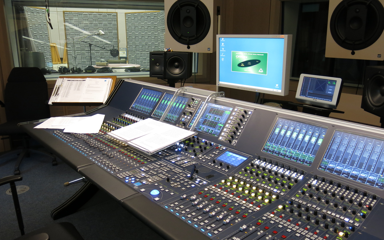 Das Foto zeigt ein Tonstudio mit Mischpult und Tonkabine im Hintergrund