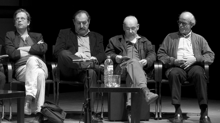 Four man are sitting next to each other on a stage