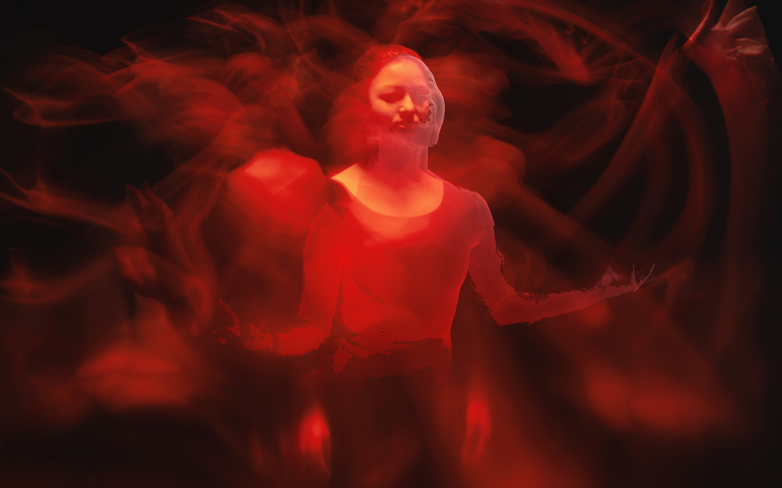 Das Foto zeigt eine von rotem Licht erleuchtete Frau in einem abgedunkelten Raum. In dieser Impression sieht man mehrere verschwommene Arme und Hände in Bewegung, die fast einer indischen Gottheit ähneln. 