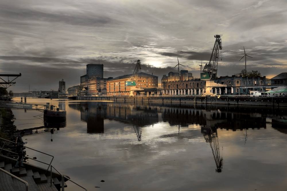 The photo shows illuminated industrial buildings along the Rhine. The sky is in gloomy evening mood.