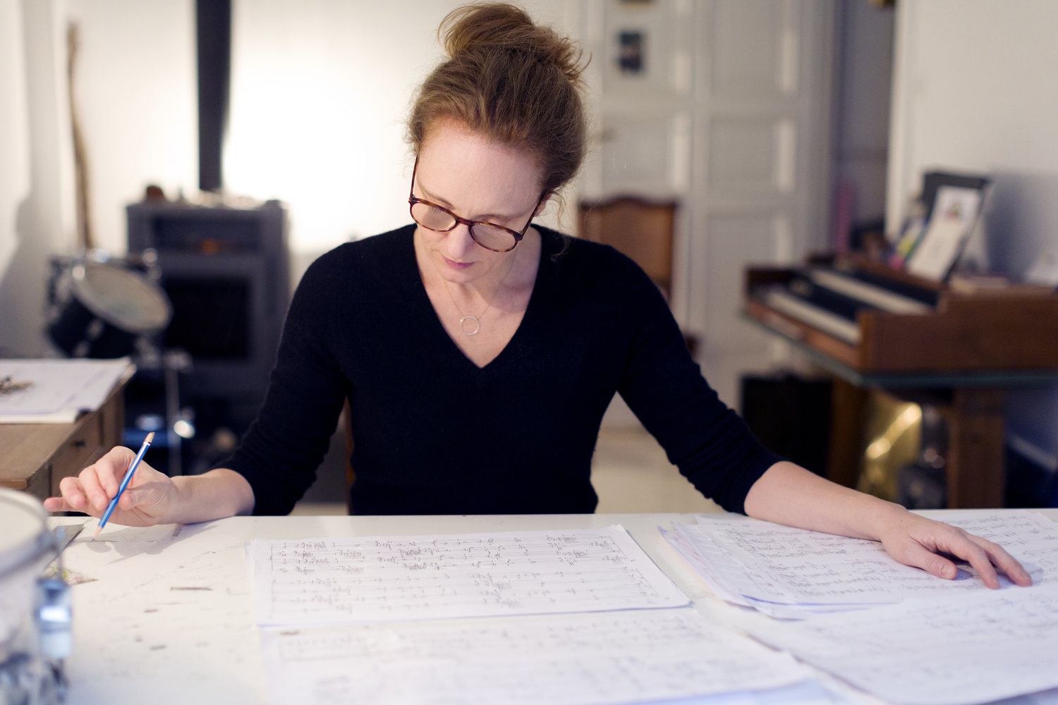 Foto einer Frau mit Brille und rötlichen Haaren, sie studiert ein Notenblatt, dass auf einem Tisch liegt.