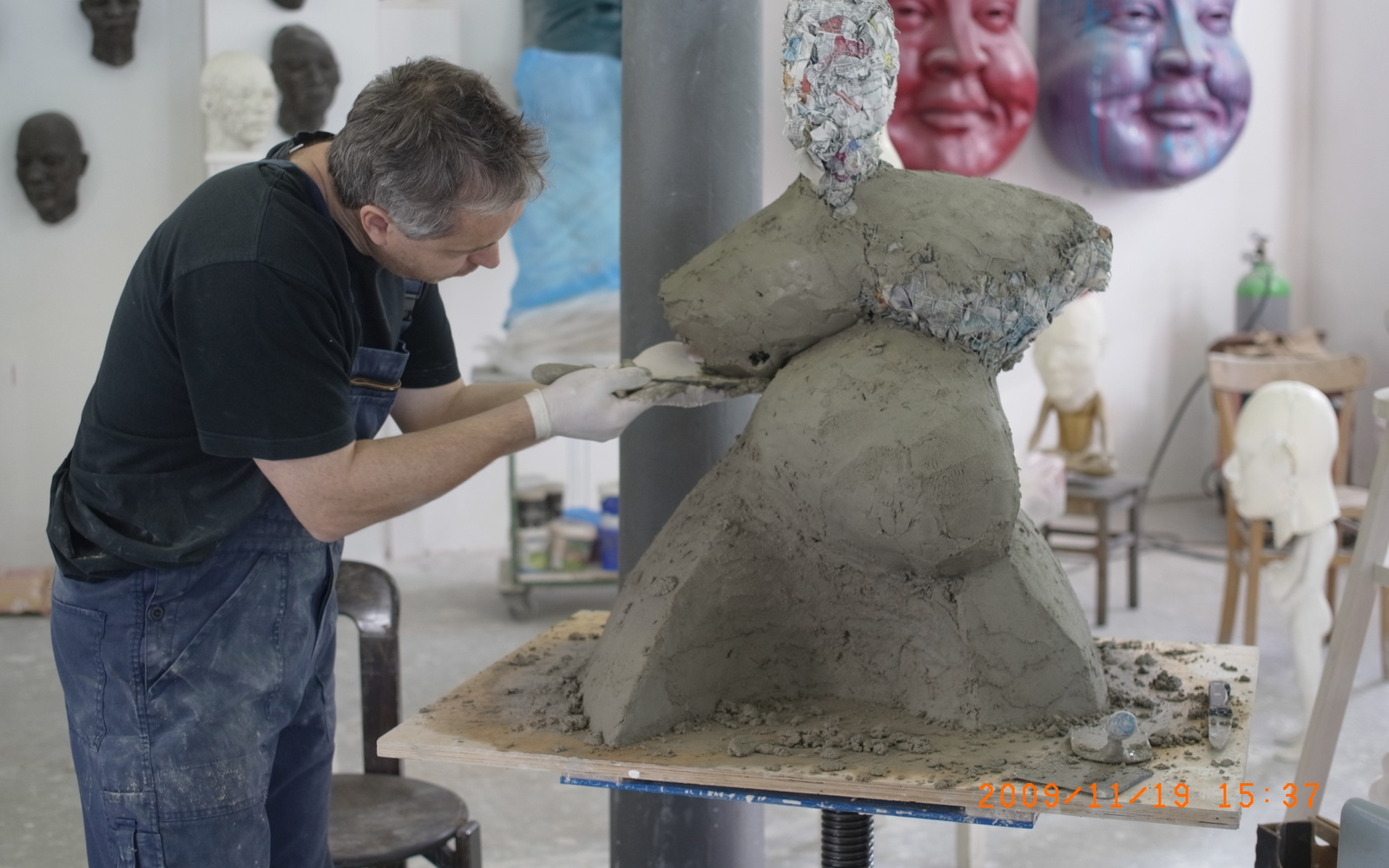 Ein Mann in Latzhosen modelliert eine voluminöse Figur aus Ton.