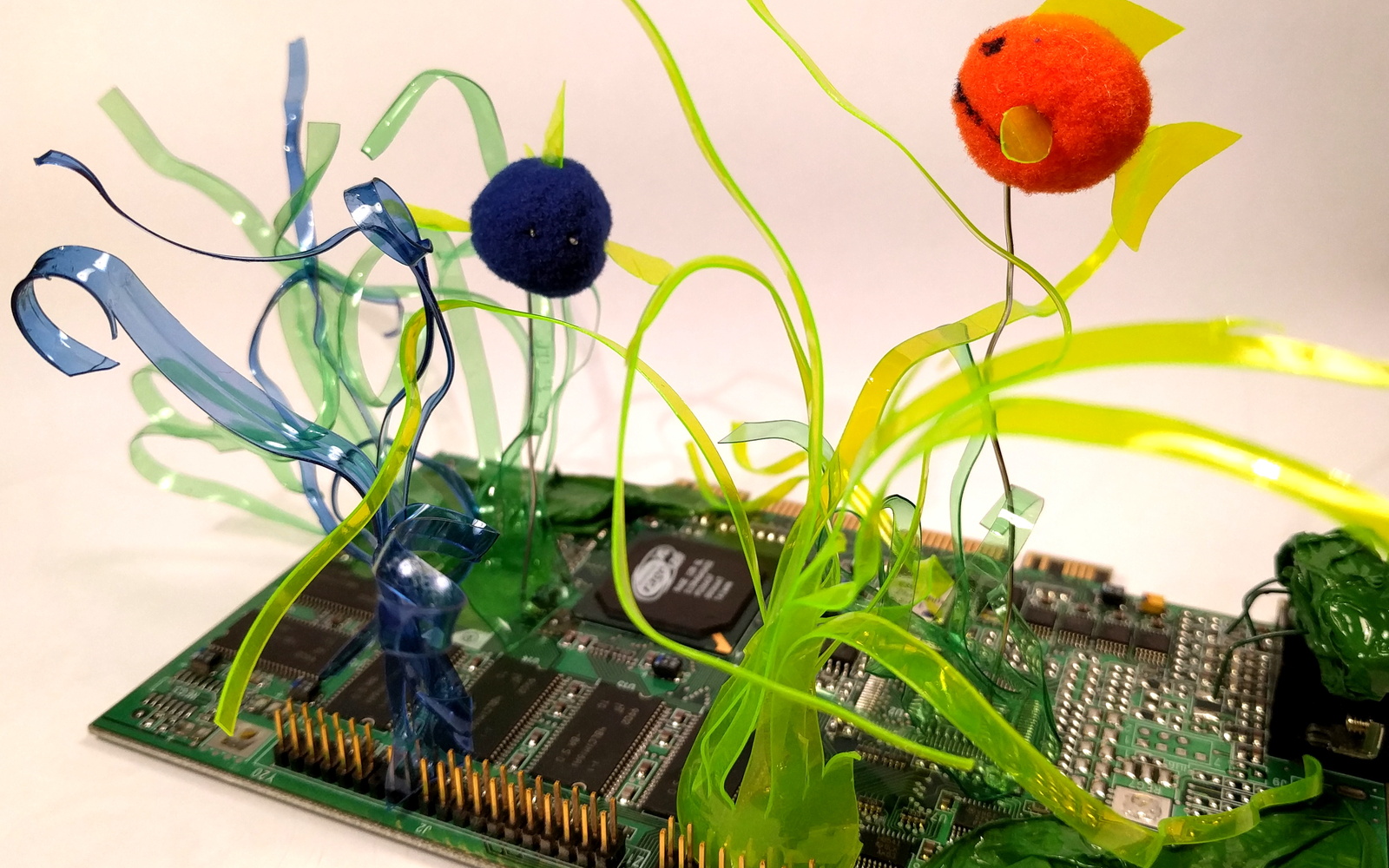 Auf einer Platine sind Blumen aus bunten PET Flaschen aufgelötet.