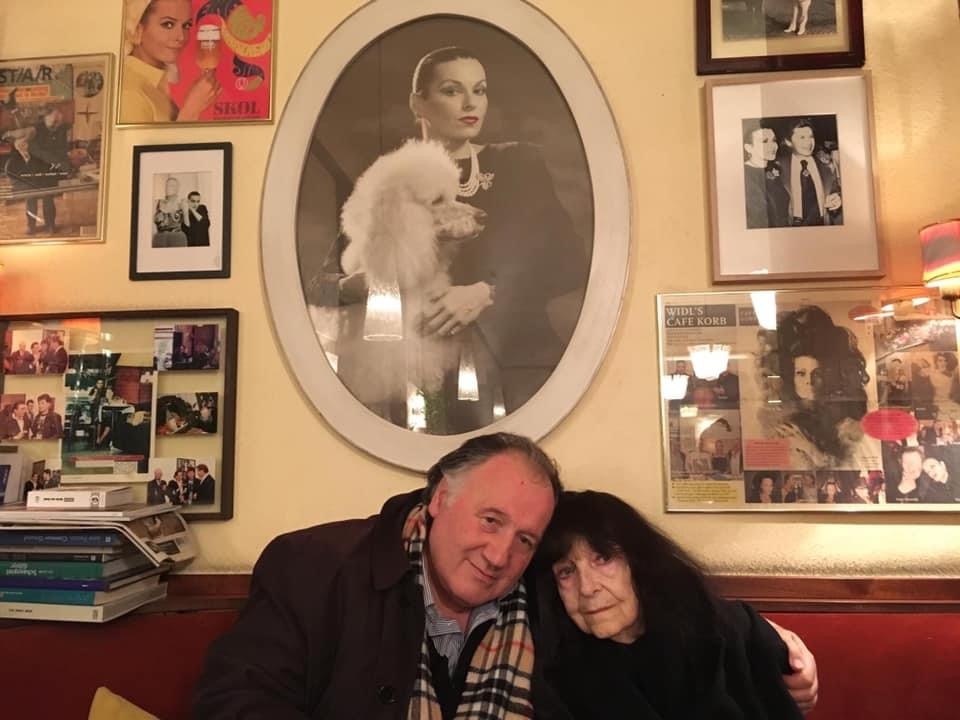Peter Weibel with Friederike Mayröcker in front of a portrait by Susanne Widl at Café Korb, Vienna 2018.
