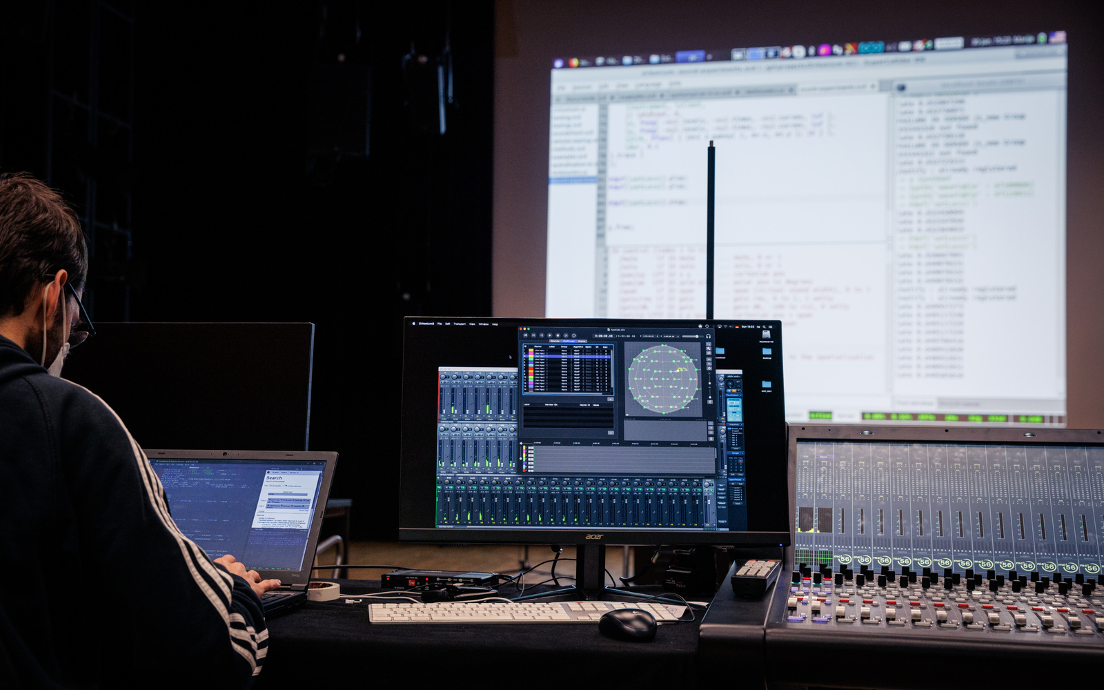 Live Coding Performance: Eine Person ist von hinten zu sehen, vor ihr ist ein Computerbildschirm und eine große Leinwand, auf der ein Programmiercode zu sehen ist.