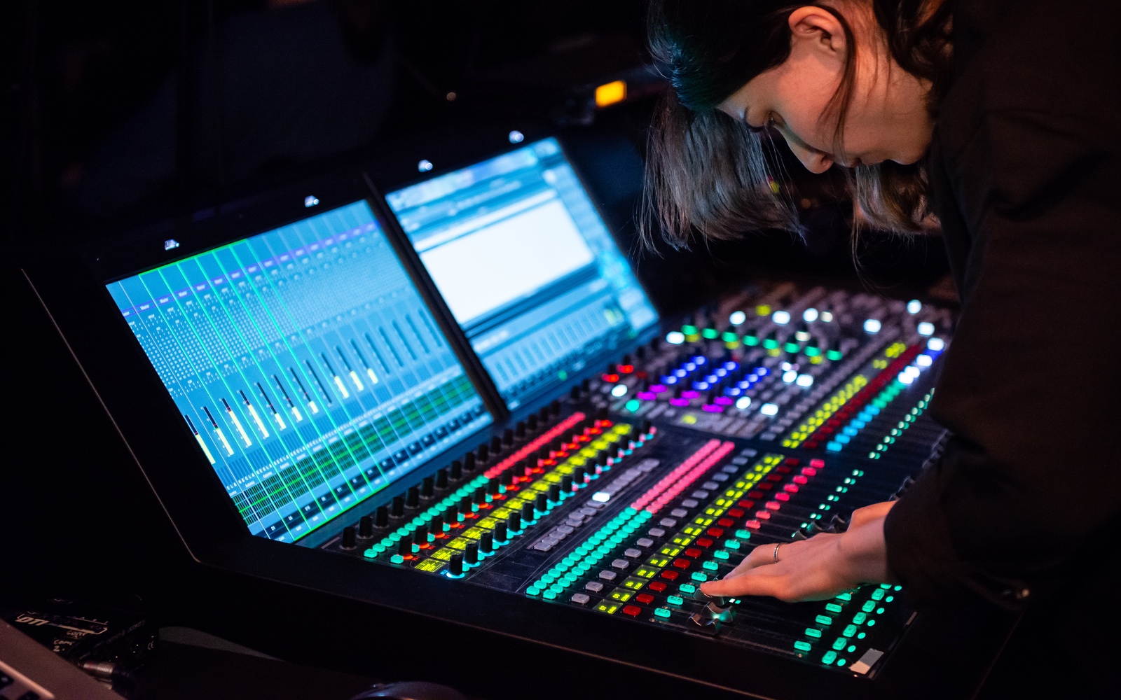You can see a woman at a large mixing console, whose controls glow in different colors.