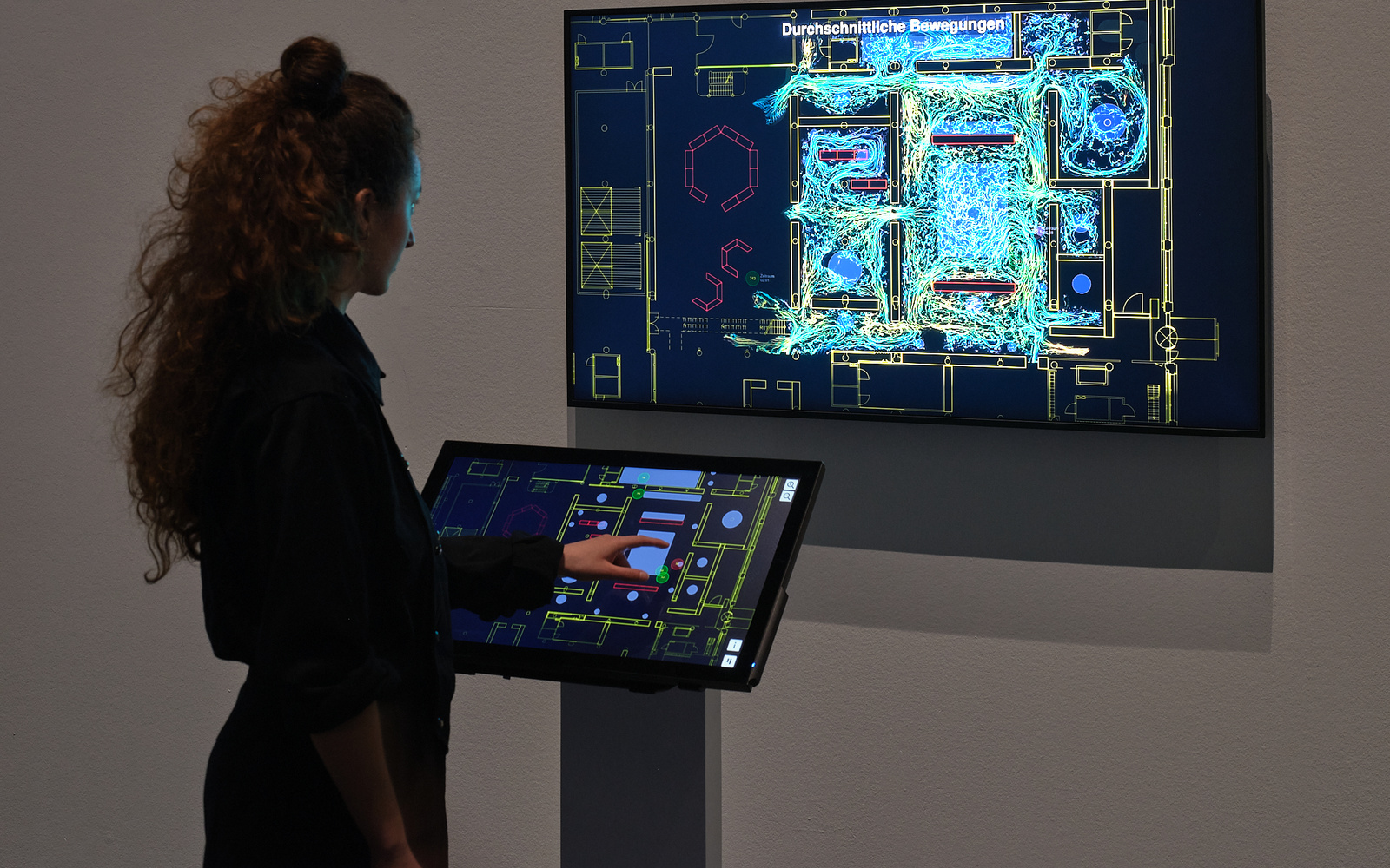 »TRACES« von Bernd Lintermann. Zu sehen ist eine Person vor einem Bildschirm, auf dem verschiedenfarbige Linien abgebildet werden. Vor der Person befindet sich ebenfalls ein Touchscreen-Bildschirm, auf dem sich ebenfalls Linien befinden. 