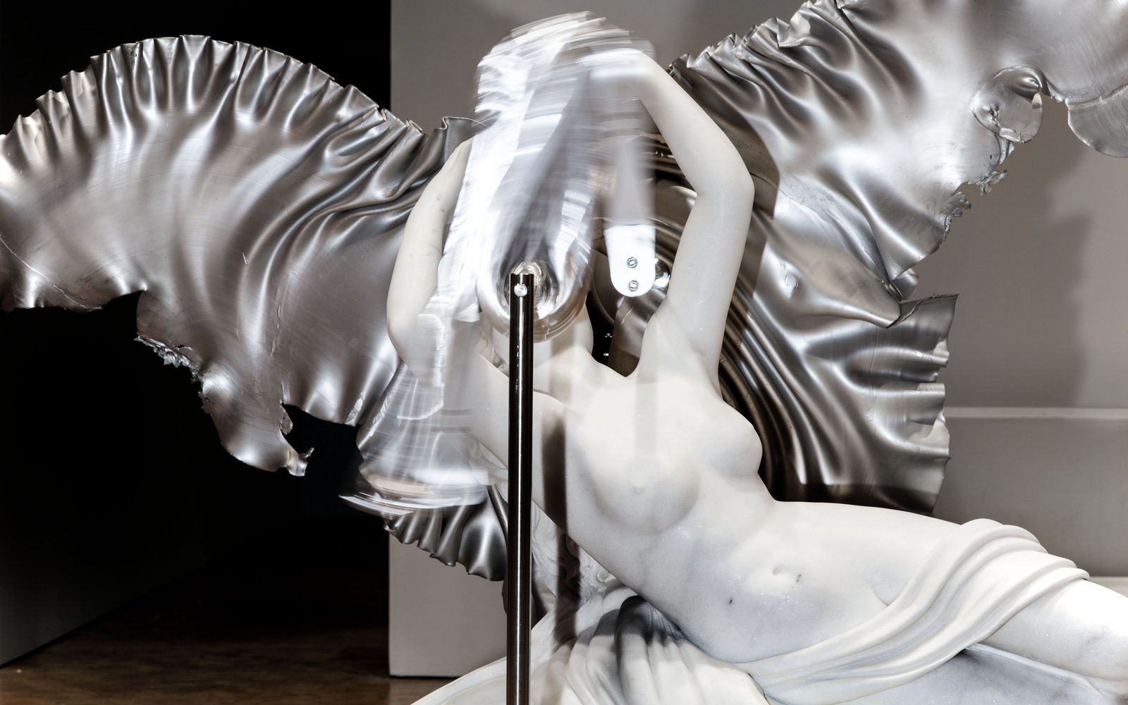 Vor dem Kopf einer klassischen Marmorstatue mit silbernen Flügeln bewegt sich unscharf eine silberne Masse.