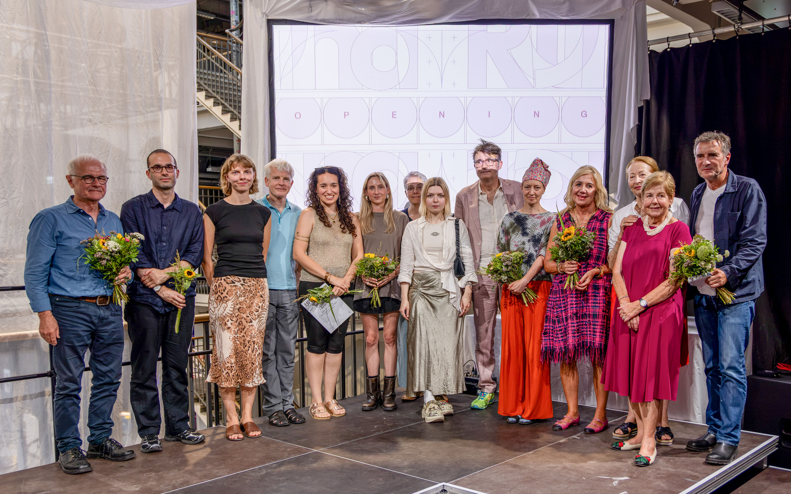 Zu sehen ist ein Gruppenbild mit mehreren Personen, die Blumen halten.