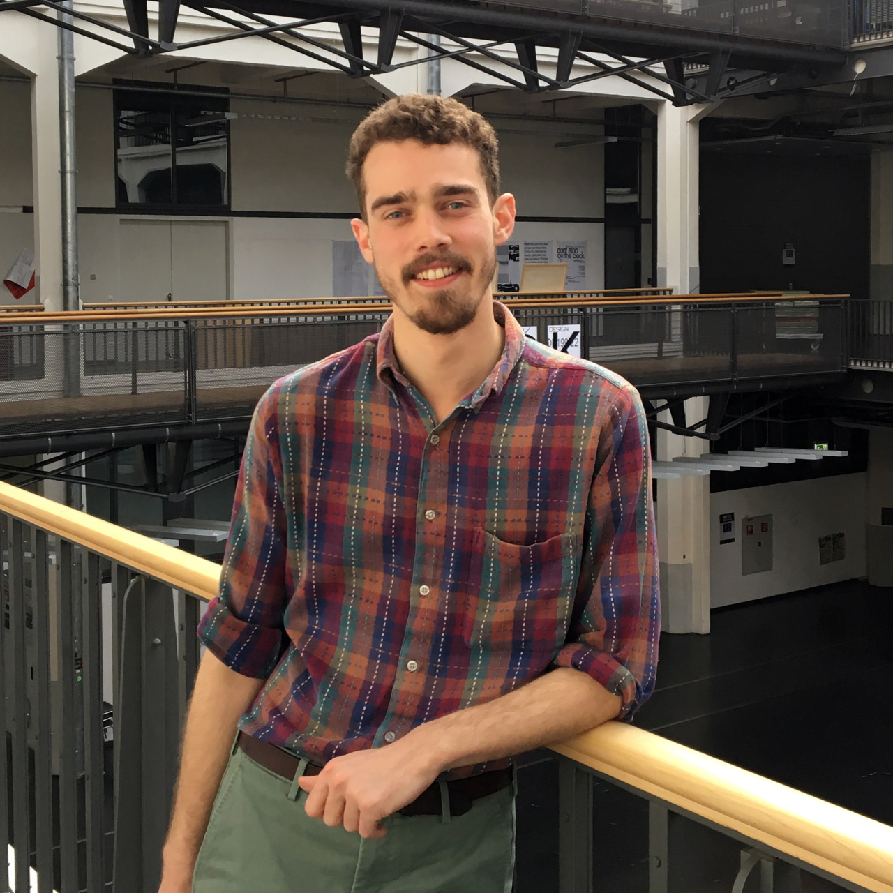 Portrait von George Barker: Ein junger Mann steht im ersten Stock des Lichthofs der HfG Karlsruhe