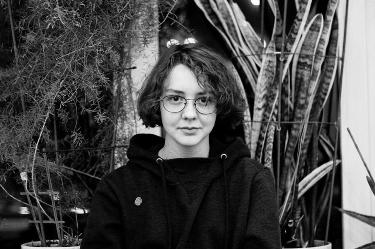 The picture shows the young curator Natasha Chychasova. It is a black and white portrait and she smiles frontally into the camera.