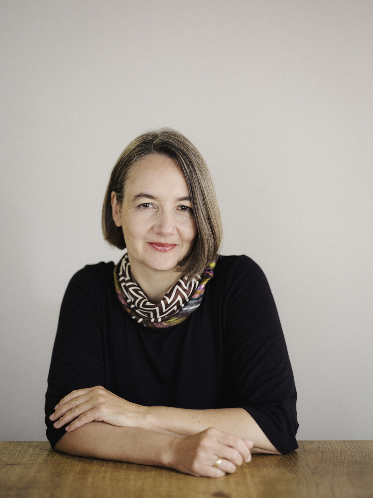 Portrait von Elke Buhr an einem Holztisch sitzend vor einer weißen Wand