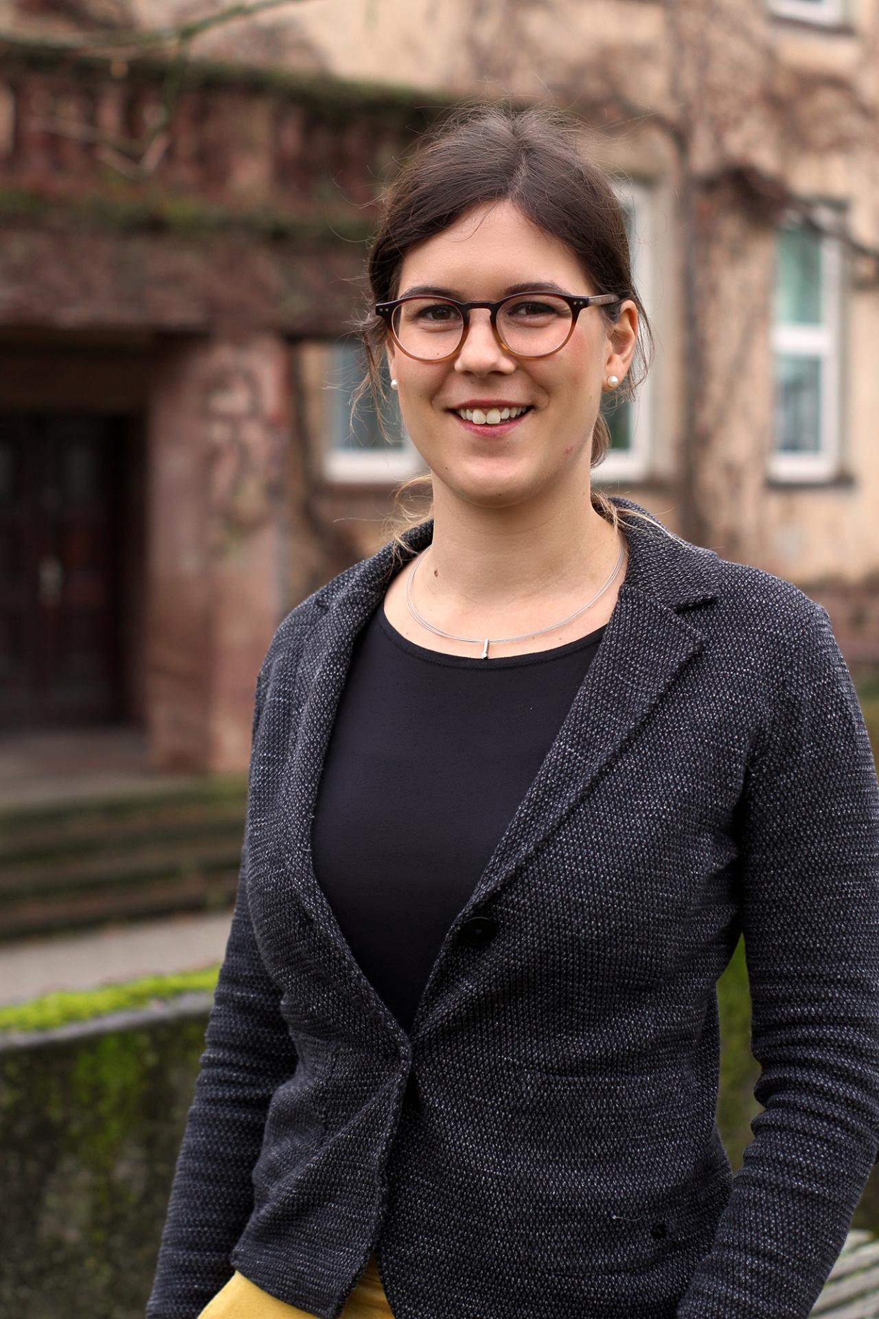 Eine Frau mit Brille, braunen Haaren und einem Blazer.