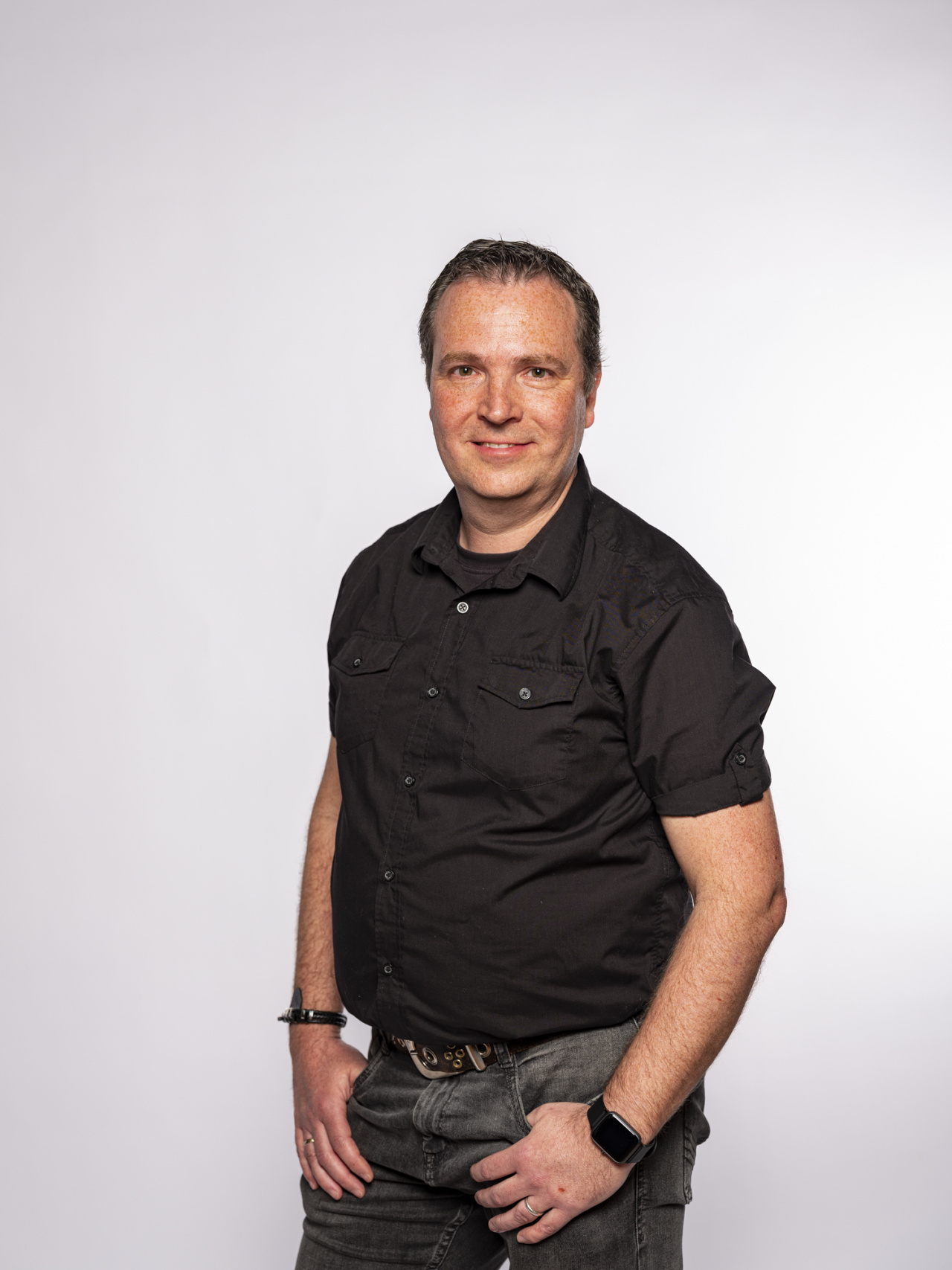 stehender Mann mit schwarzem Hemd und die Hände in der Hosentasche