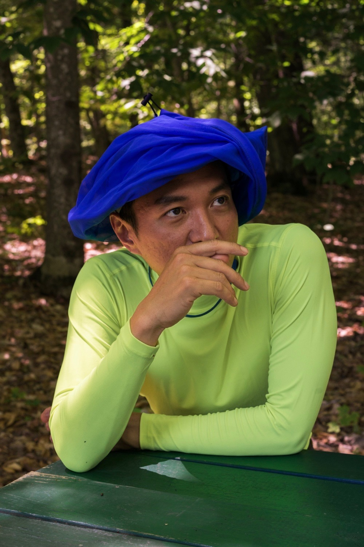 zu sehen ist ein Mann in grünem langen Shirt und einem blauen Turban, er stützt sein Kopf auf einer Hand ab und schaut, rechts aus dem Bild