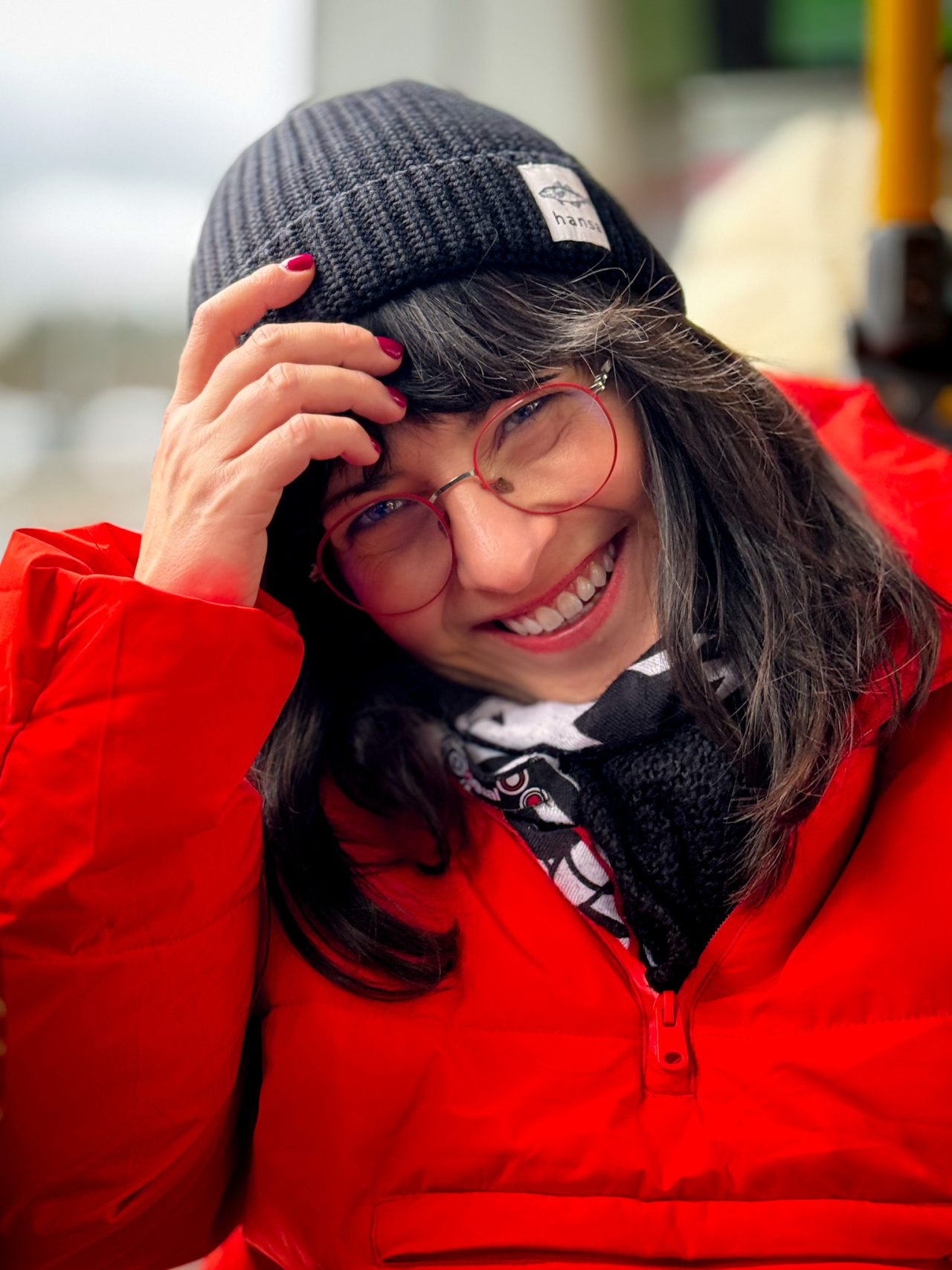 A smiling woman in a woolly hat wearing a thick red jacket.