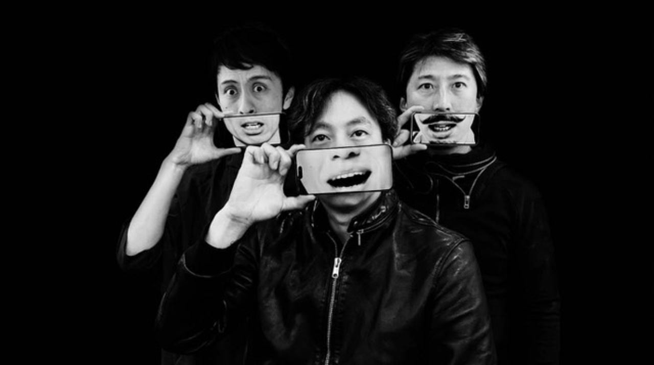Three people in a white-and-black photo are each holding a cell phone in front of the lower half of their faces.