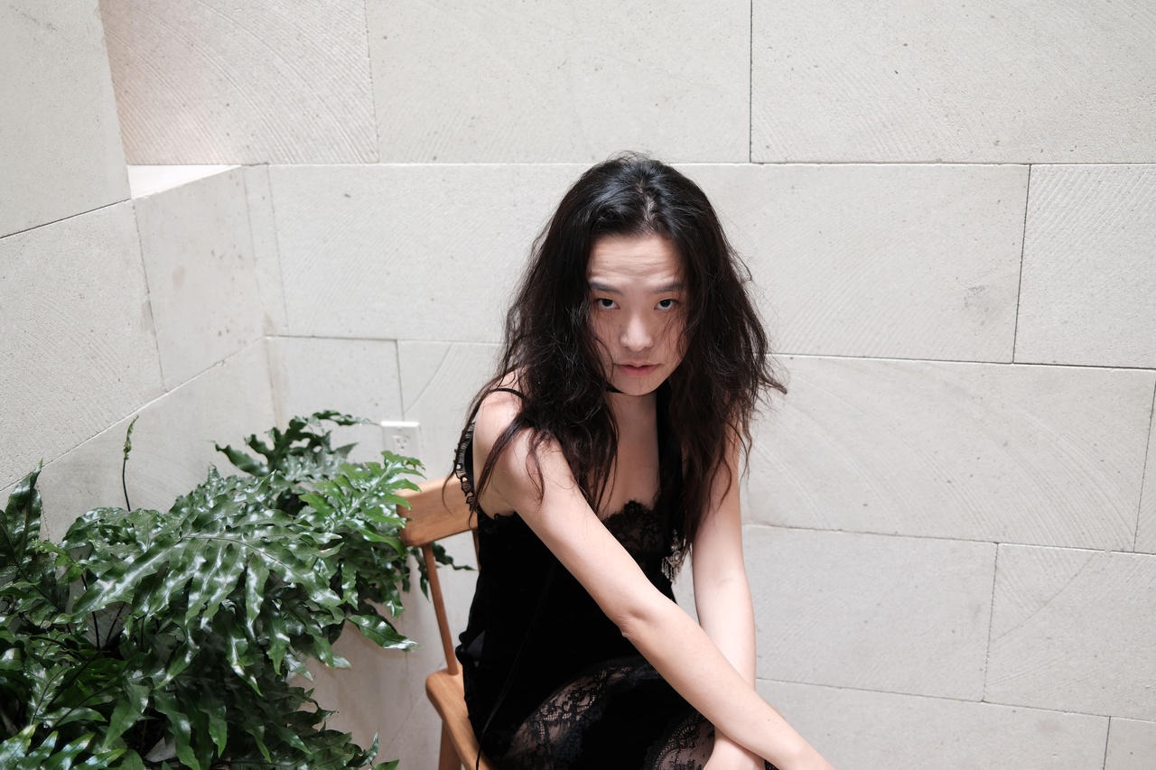 A portrait photo of a person in front of a concrete wall with a plant.