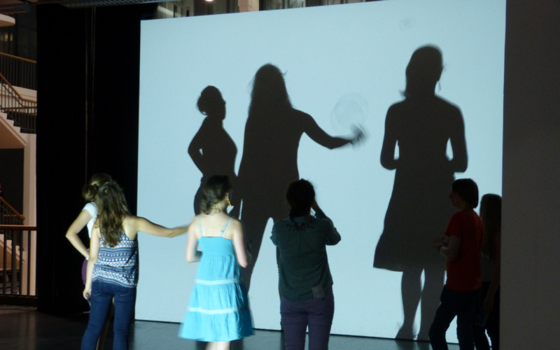Children are standing in front of a wall where there shadows fall