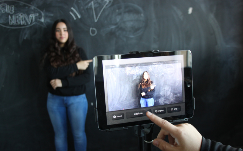 Ein Mädchen, das vor einer Tafel steht, wird mit einem Tablet fotografiert.