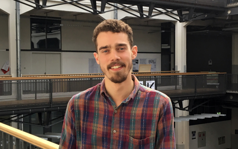 Portrait von George Barker: Ein junger Mann steht im ersten Stock des Lichthofs der HfG Karlsruhe