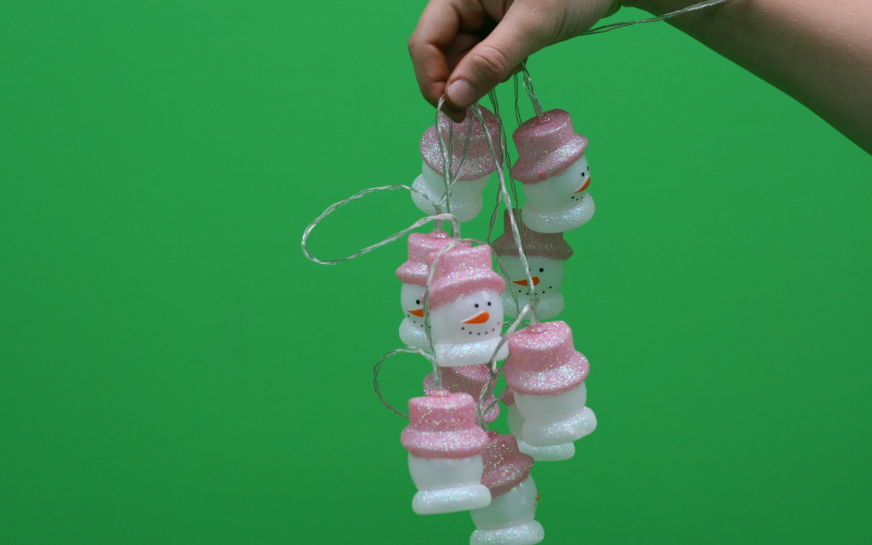 Eine Schneemänner-Lichterkette wird vor einem Greenscreen gehalten.