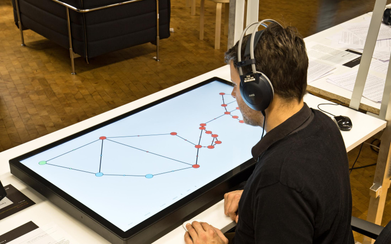 A man has headphones on and sits in front of a large screen lying on the table, which shows a graphic structure