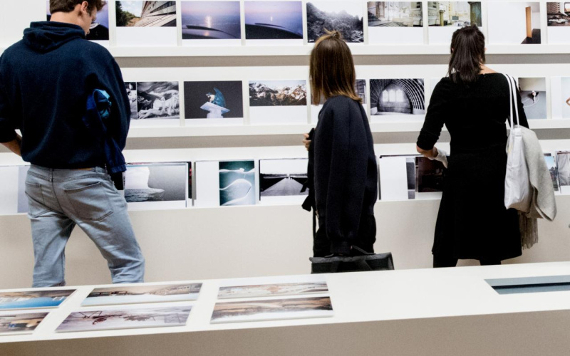 Three people view photographs in an exhibition