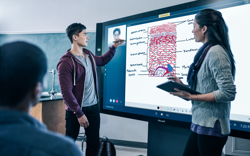 A man and a woman are standing in front of a big screen