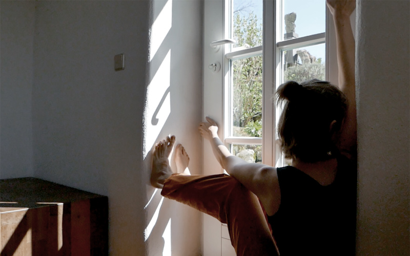 Zu sehen ist eine Person, die auf der Innenseite des Fenstersims sitzt und aus dem Fenster sieht.