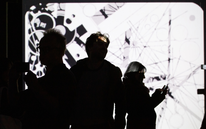 Foto von Menschen vor einer Leinwand mit einem abstrakten Video in Schwarz-Weiß – Eine Impression der Ausstellung »bauhaus.film.expanded« am ZKM Karlsruhe.